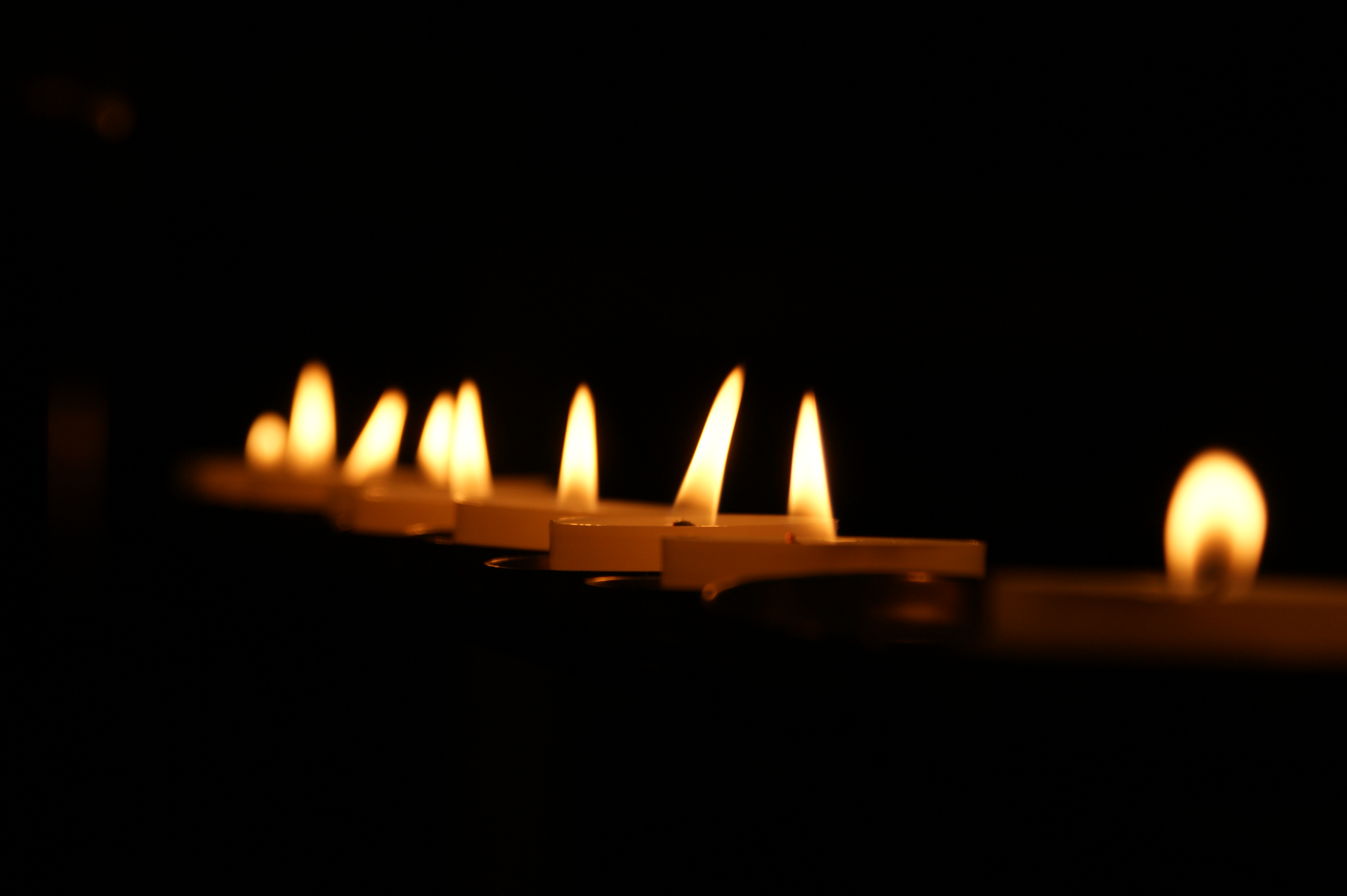 A line of small votive candles flicker against a black background.